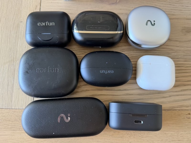 eight TWS cases for size comparison — three EarFun, H3, two Viaim, AirPods, Status Pro X