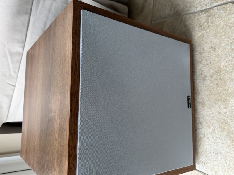 the subwoofer from an angle, showing the front grille and wood-finish cabinet