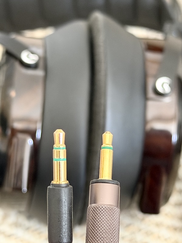 two 3.5mm cable plugs held against the earcups — the left socket takes a two-ring plug, the right socket needs a single-ring plug
