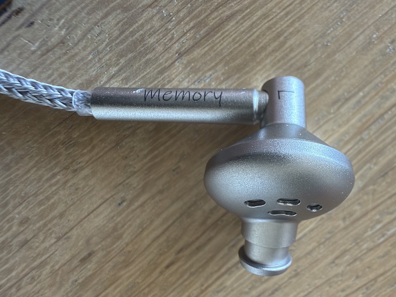 top-down view of the L earpiece showing the rear vent holes and the Memory-branded cable barrel